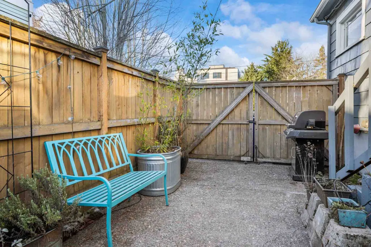 An inviting outdoor area featuring a turquoise bench, grill, potted plants, and a sturdy wooden fence. The bench faces a cozy corner ideal for unwinding or reading, while the grill promises fun and delicious meals outdoors. Vibrant plants and the securely fenced perimeter evoke both relaxation and a pet-safe environment.