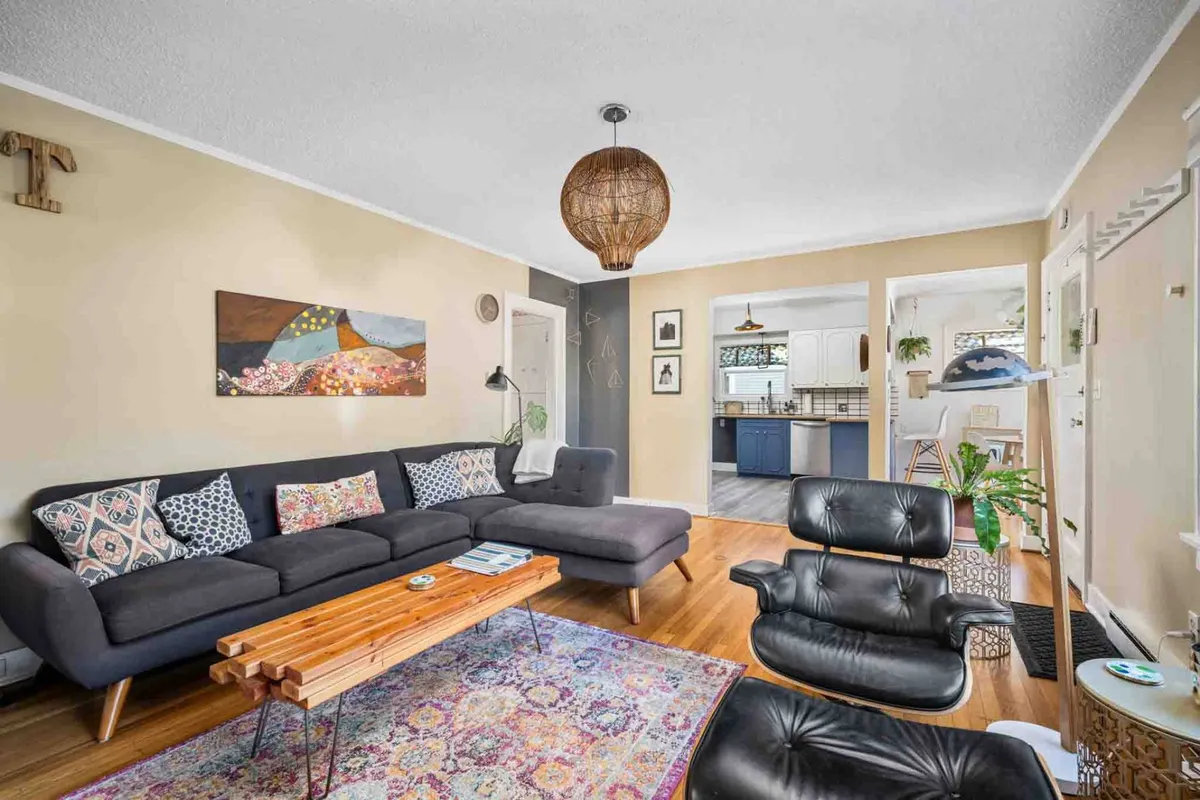 A comfortable living room scene featuring a mid-century style sofa, a central coffee table, striking wall artwork, and a stylish pendant light. Natural light streams into the room, illuminating the seating area and highlighting the inviting ambiance.