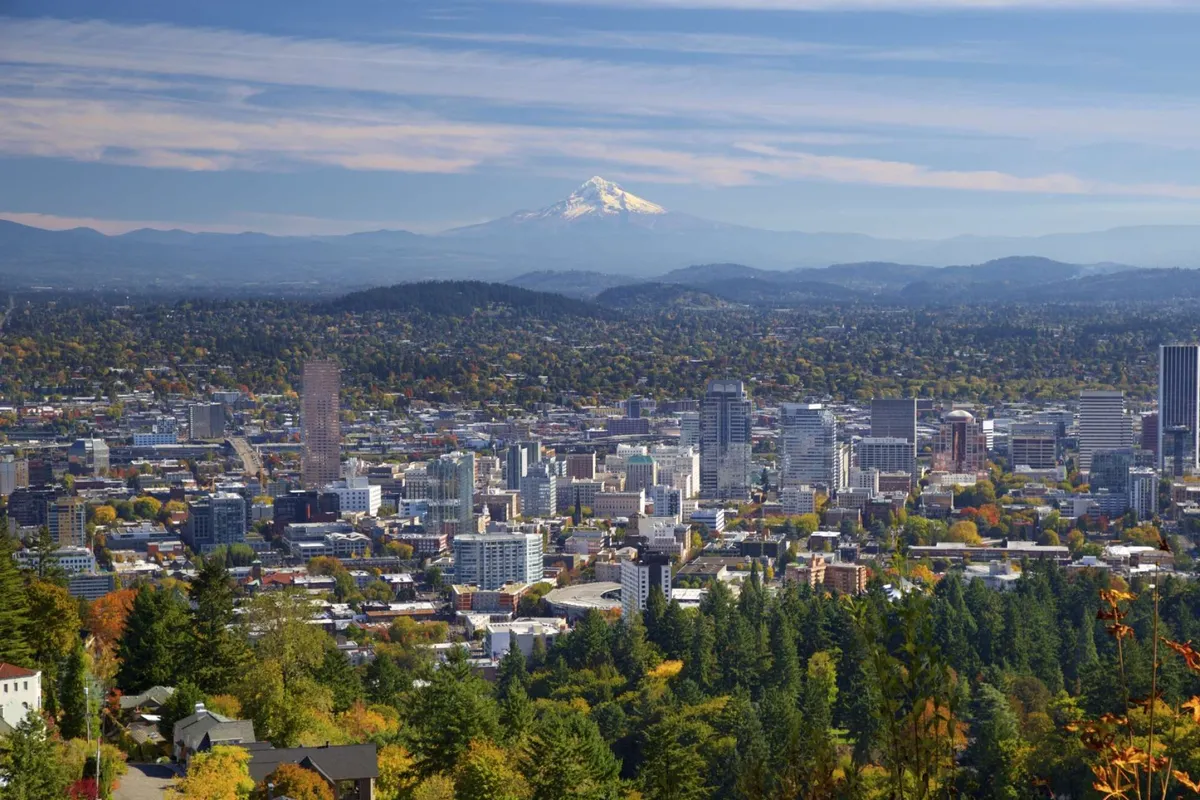 A panoramic view showcasing Mount Hood in the distance, lush greenery, downtown Portland, and vibrant autumn foliage. The image captures the intersection of urban life and natural beauty, emphasizing the city's proximity to parks and outdoor exploration.