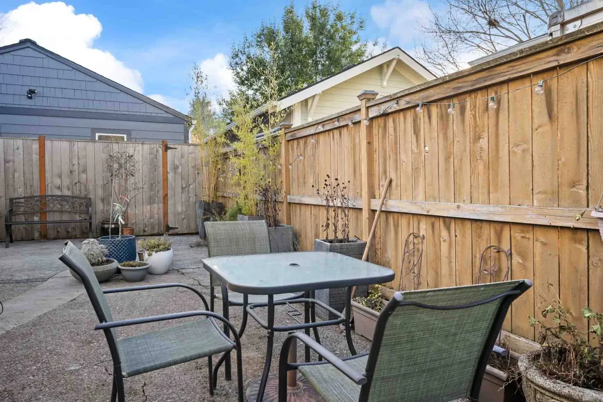 A peaceful backyard scene with a table and chairs set on a lush green lawn, surrounded by a wooden fence. Potted plants and flowers add color and vibrancy, while the fence ensures privacy and safety for children or pets at play. The scene is inviting, portraying a tranquil space perfect for relaxing or gathering with loved ones.