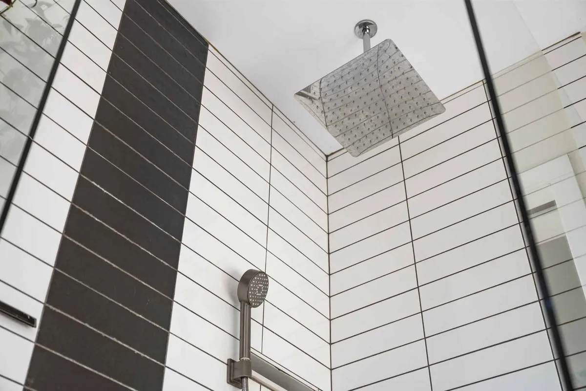 A modern bathroom with a ceiling-mounted rain showerhead, striped tiles, and a glass enclosure. The scene exudes a spa-like ambiance, promising a luxurious and refreshing shower experience.